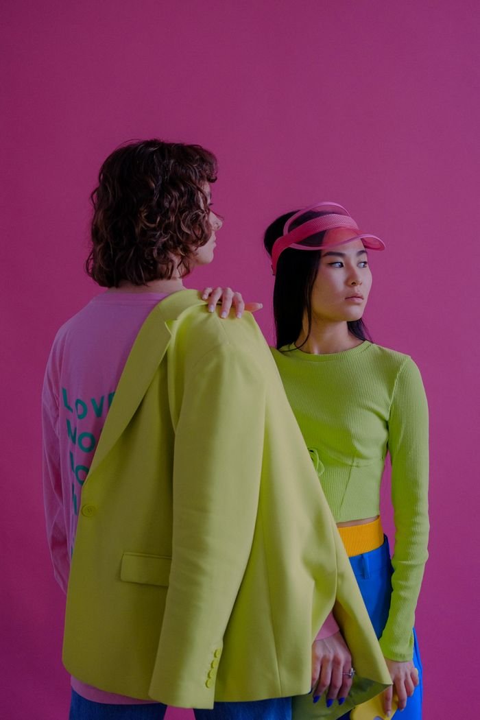 gallery-5 Colorful fashion portrait of two people in dynamic poses against a pink background.