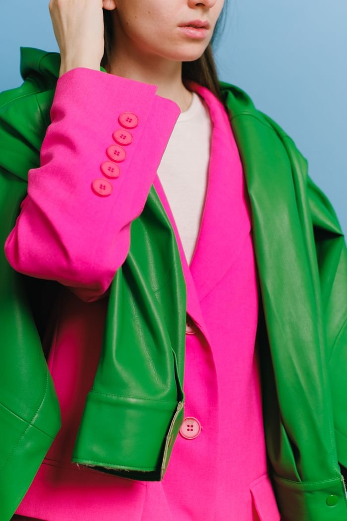 gallery-6 Fashionable woman wearing a vibrant pink blazer and green jacket, exuding modern style.