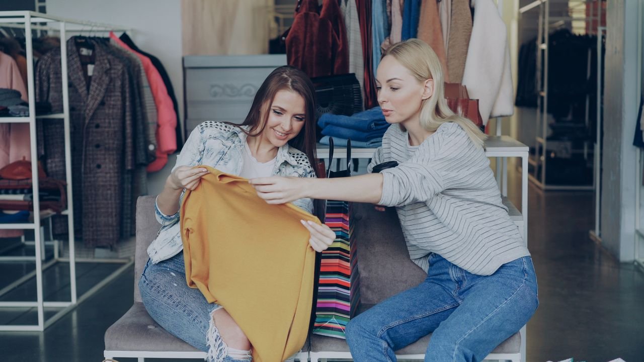 services-02 Two women shopping and examining clothes in a fashion boutique, enjoying their retail experience.