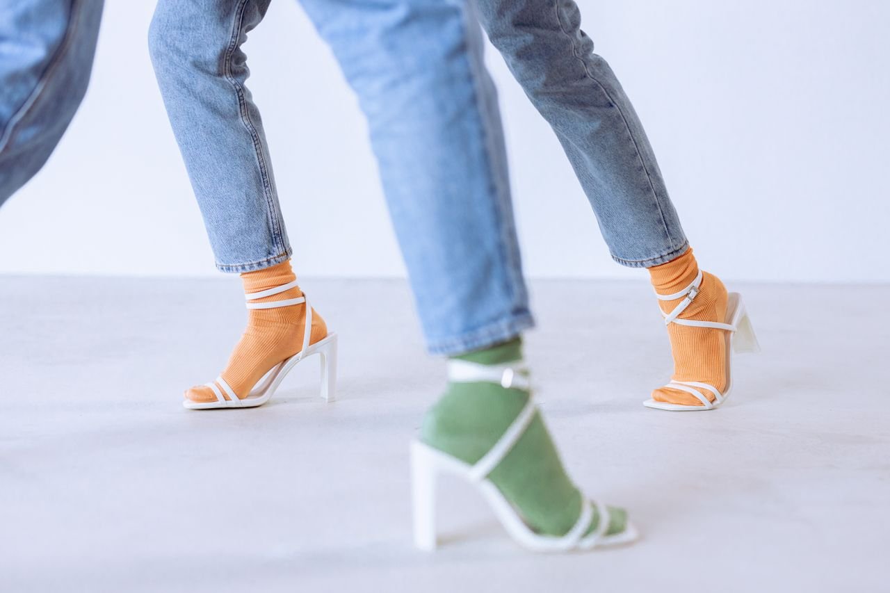 why-choose-us Stylish heeled sandals with colorful socks paired with denim jeans in a studio setting.