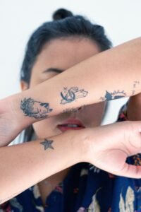 woman getting a fine line floral tattoo on her forearm in a tattoo studio