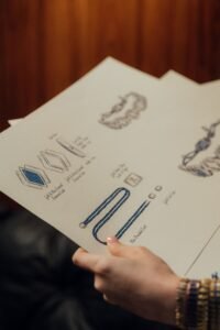 hand sketching a custom engagement ring design on paper next to loose gemstones