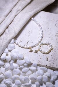 flat lay of sterling silver studs, a thin gold bracelet and a pearl necklace on a white surface
